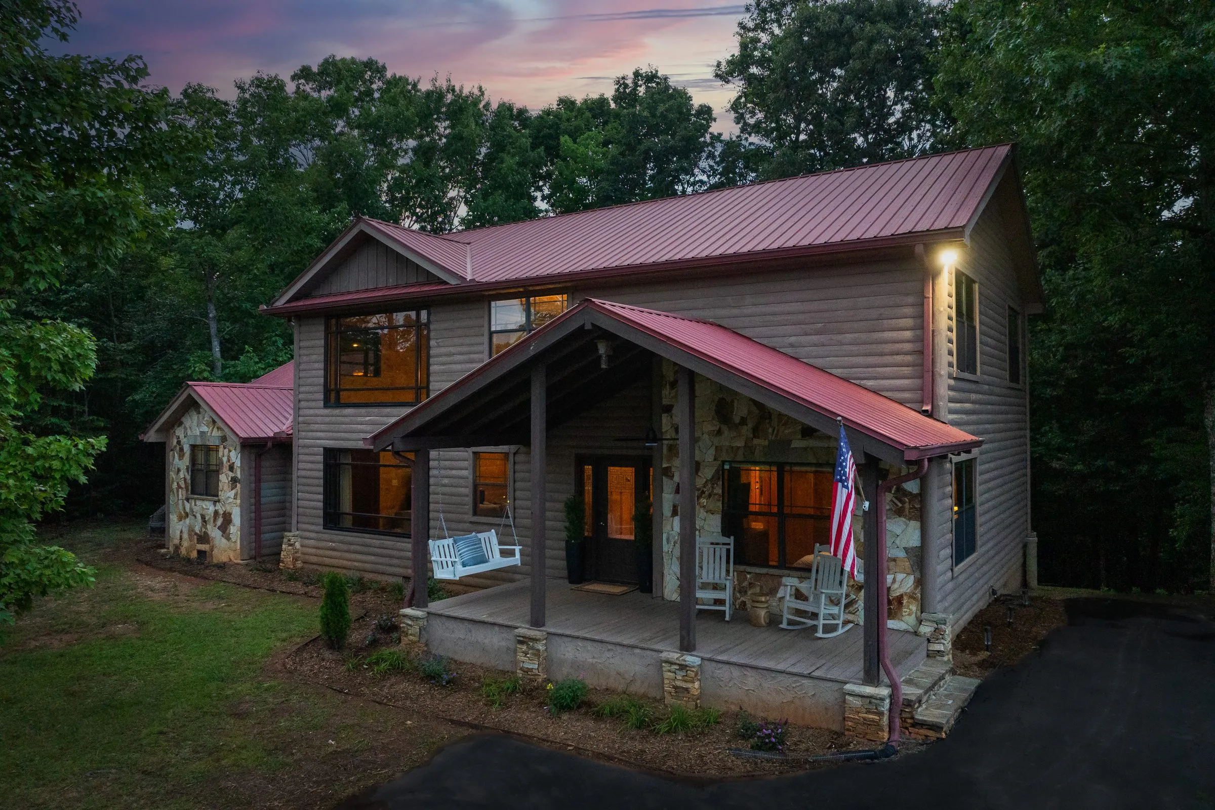 Monarch's Roost cabin at dusk with lit windows, red metal roof and covered porch
