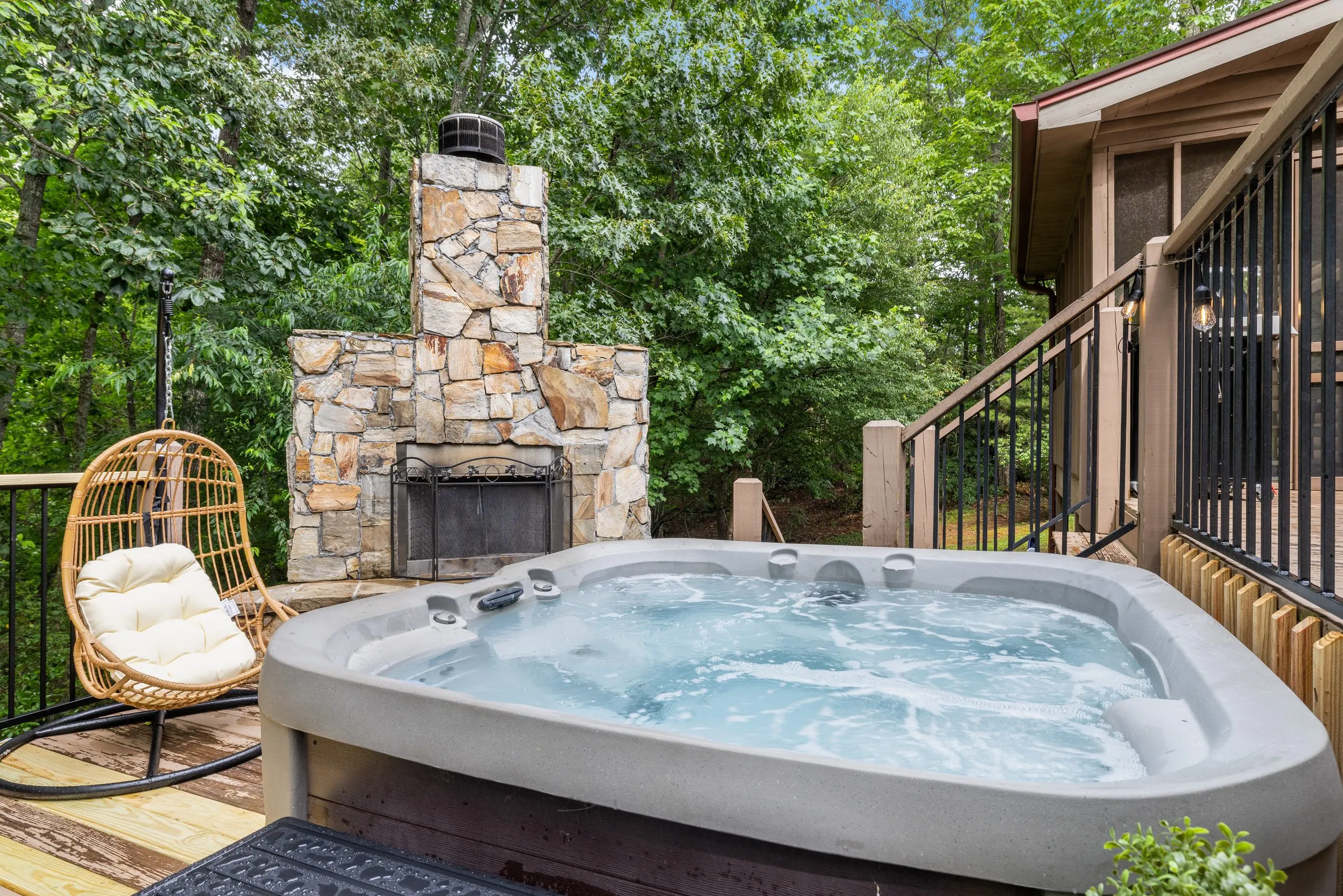 Hot tub beside the outdoor stone wood-burning fireplace and a hanging egg chair