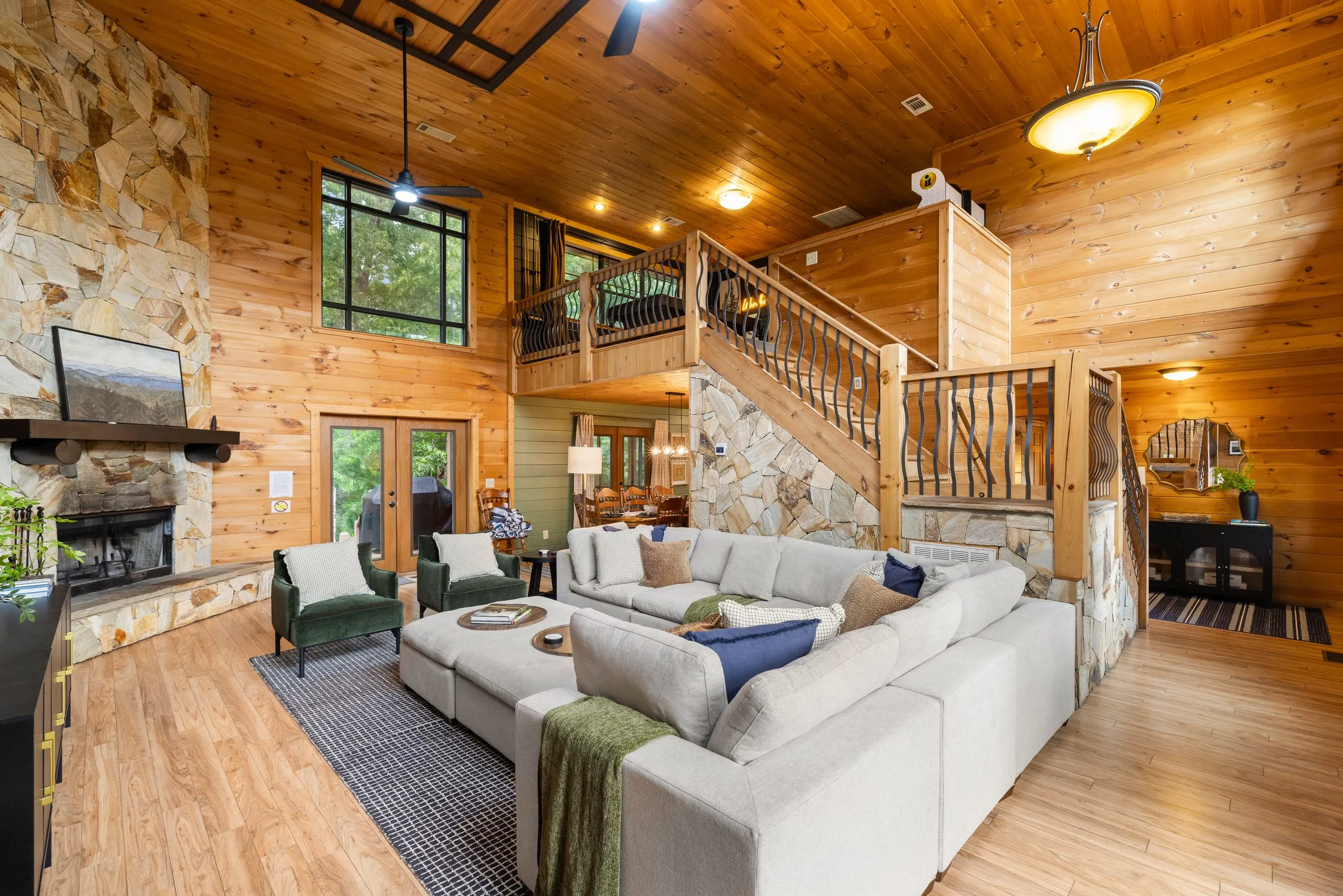 Living room and loft staircase with a stone fireplace and open dining beyond