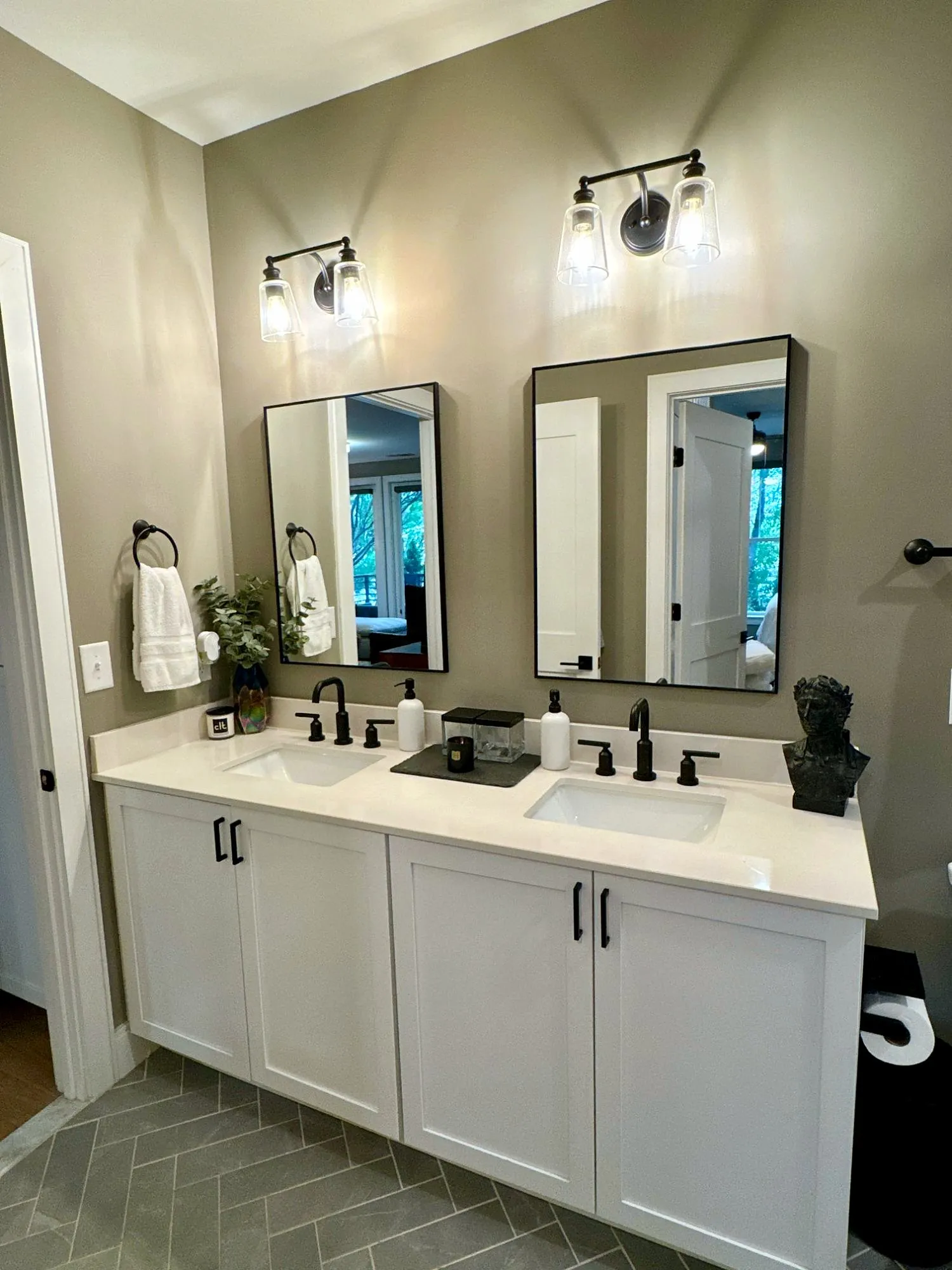 Bathroom with a double white vanity, two black-framed mirrors, black fixtures and herringbone slate floor tile