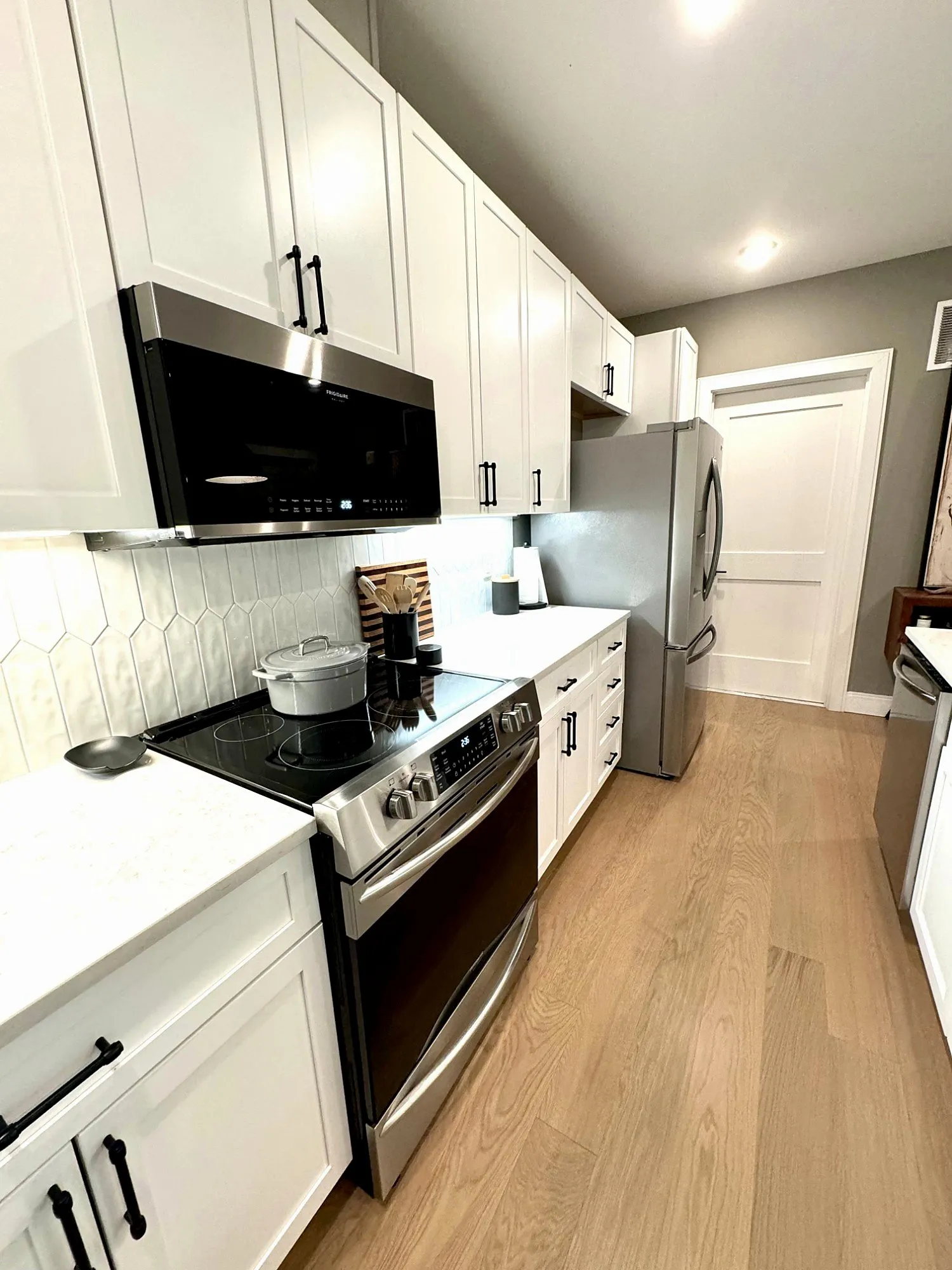 Galley kitchen with white shaker cabinets, a pale tile backsplash, glass cooktop and stainless refrigerator