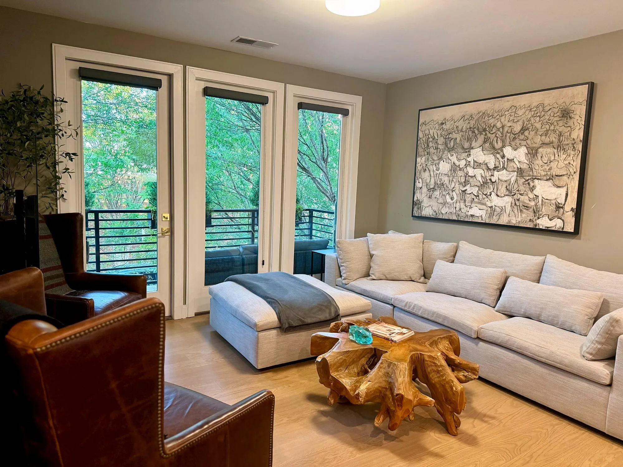 Living room with a large light sectional, teak root coffee table, leather armchairs and tall glass doors opening to the patio