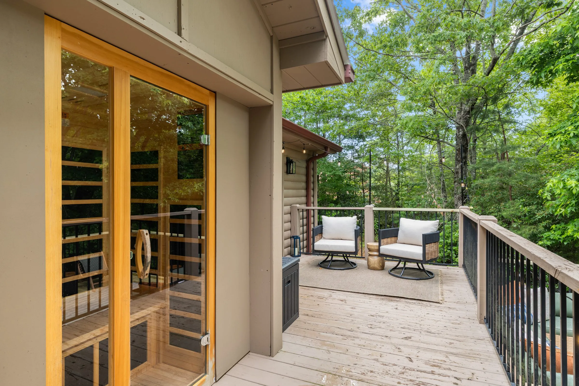 Glass door of the outdoor infrared sauna on the deck with swivel chairs and forest behind